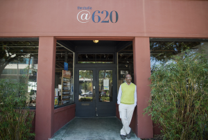 A man standing at a building entrance. He is leaned against a column, with his hands in his pockets.